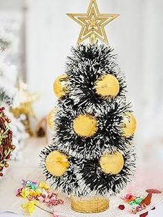 a small christmas tree decorated with yellow and black balls is sitting on a white table