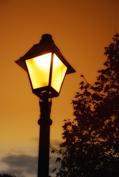 a street light with the sun setting in the background and trees silhouetted against an orange sky