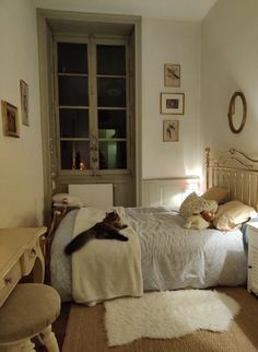 a cat laying on top of a bed next to a desk and chair in a bedroom