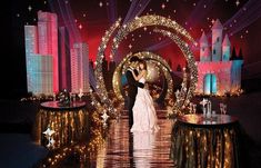 a bride and groom standing in front of a stage decorated with christmas lights at night