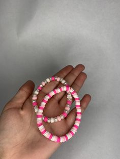 a hand holding two bracelets with pink and white beads