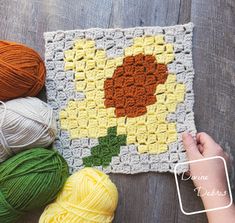 a crocheted square with flowers on it and balls of yarn next to it