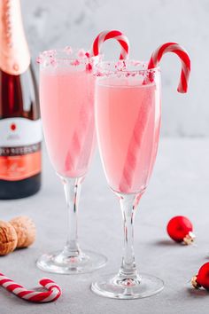 two glasses filled with pink liquid next to a bottle of champagne and candy canes