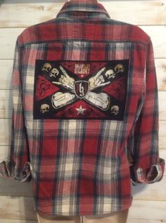 a red and black flannel shirt with skulls on the chest is hanging up against a wooden wall