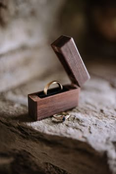 an open wooden box with two wedding rings in it on top of a stone surface