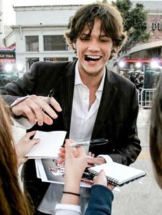 a young man in a suit signing autographs for some people on the street outside