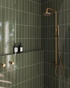 a green tiled bathroom with shower head and soap dispenser