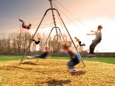 three children playing on a swing set in an open field with the sun behind them