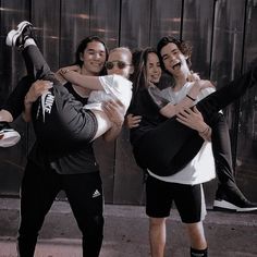 a group of people standing next to each other in front of a wooden wall with their arms around one another