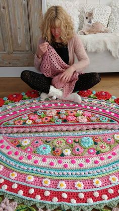 a woman sitting on the floor with a crocheted rug in front of her