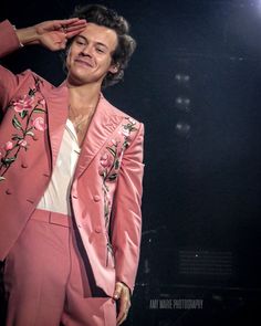 a male in a pink suit is holding his hand up to his ear and looking at the camera