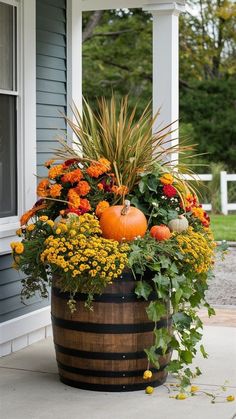 a wooden barrel filled with lots of flowers and pumpkins on the front porch next to a house