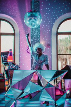 a woman standing in front of a disco ball and mirror sculpture with her arms up