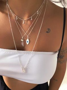 a close up of a woman wearing a white top with multiple necklaces on her chest