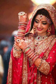 a woman in red and gold bridal outfit holding her hands up to her face