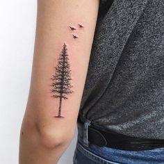 a woman's arm with a small pine tree tattoo on the left upper arm