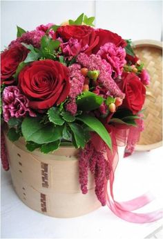 a basket filled with red and pink flowers on top of a white table next to a straw hat