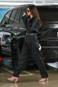 a woman in high heels walking past a black suv with her hand on her hip