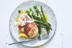 a white plate topped with meat and asparagus next to lemon wedges on a table