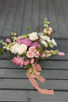 a bouquet of flowers sitting on top of a wooden floor next to a pink ribbon