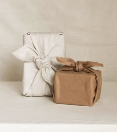 two wrapped presents sitting next to each other on top of a white tablecloth covered surface