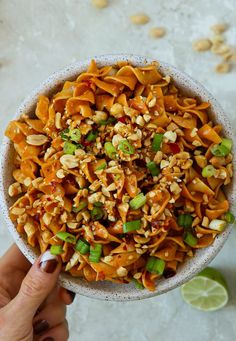 a person holding a bowl full of food with nuts and green onions on the side