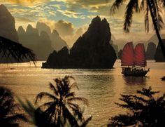 a red sailboat in the ocean with mountains and clouds behind it at sunset or dawn