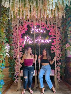 two women sitting on swings in front of a floral backdrop with the words hola mimos