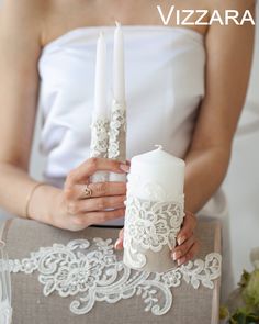 a woman holding two white candles on top of a table