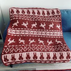 a red and white knitted blanket sitting on top of a blue couch next to a wooden table