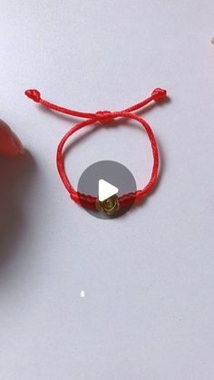 a red string bracelet with a gold button on it next to an orange plastic object