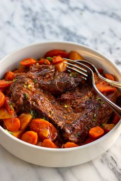 a white bowl filled with meat and carrots on top of a marble countertop