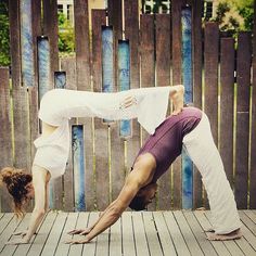 two people doing yoga poses on a wooden deck