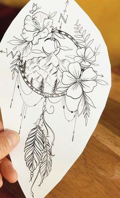 a person holding up a piece of paper with flowers and feathers on it