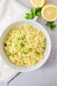 a white bowl filled with rice and garnished with parsley next to sliced lemons