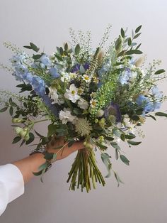 a bouquet of blue and white flowers being held by a person's hand in front of a wall