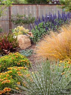 a garden filled with lots of different types of flowers and plants next to a wooden fence