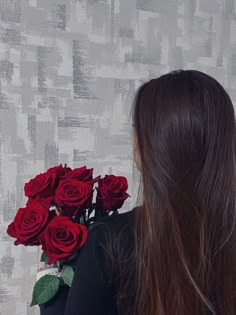 a woman with long brown hair and red roses in her hand, looking at the wall