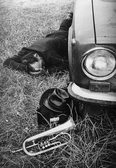 a man laying on the ground next to a car with a trumpet in front of it