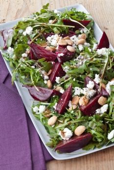 beet salad with goat cheese and almonds on a white platter next to a purple napkin