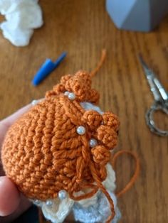 an orange crocheted object being held by someone's hand on a wooden table