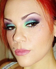 a woman with bright red hair and blue eyeshadow is looking at the camera