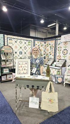 a woman sitting at a table in front of quilts on display with bags around her