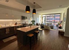 an open kitchen and living room area with wood flooring, large windows, and modern furnishings