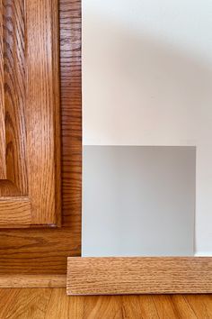 the corner of a room with wood flooring and white walls, next to a wooden door