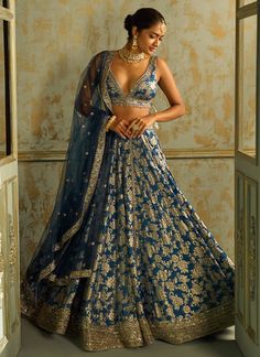 a woman in a blue and gold lehenga standing by an open door with her hands on her hips