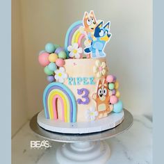 a birthday cake decorated with cartoon characters and rainbows on a white pedestal in front of a wall