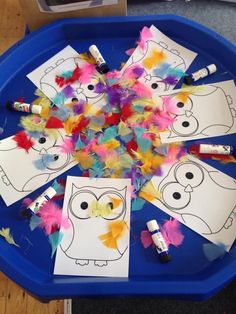 paper owls and feathers on a blue tray with crayons in the middle, surrounded by markers