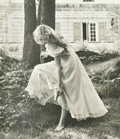 an old black and white photo of a woman kneeling in the grass near a tree