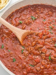 a wooden spoon in a pot filled with spaghetti and meat sauce on a white surface